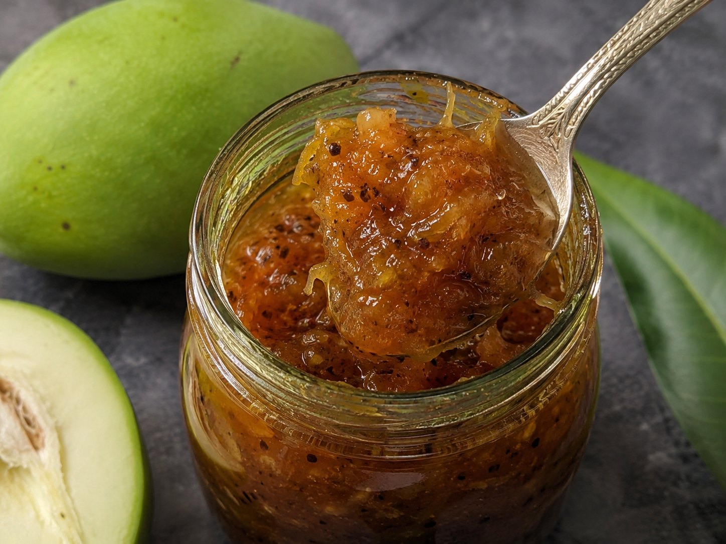 Homemade raw mango jam with jaggery, misri, cardamom, and dry ginger in a glass jar