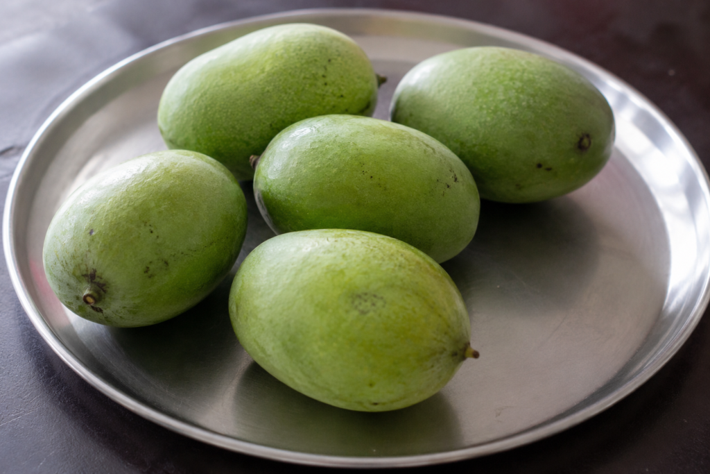Five raw mangoes on a steel plate